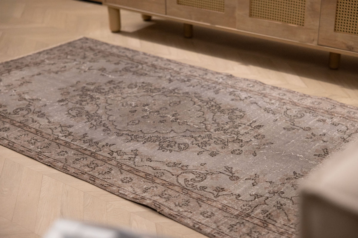 Hand-woven vintage gray overdyed Isparta Turkish wool and cotton rug with intricate floral patterns on a wooden floor.