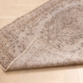 Vintage gray overdyed Isparta Turkish wool and cotton rug with floral patterns and a folded corner on a wooden floor.