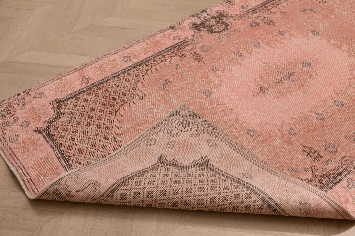 Vintage 3x6 ft pink overdyed Turkish Isparta rug with floral patterns, hand-woven from wool and cotton on a wooden floor.