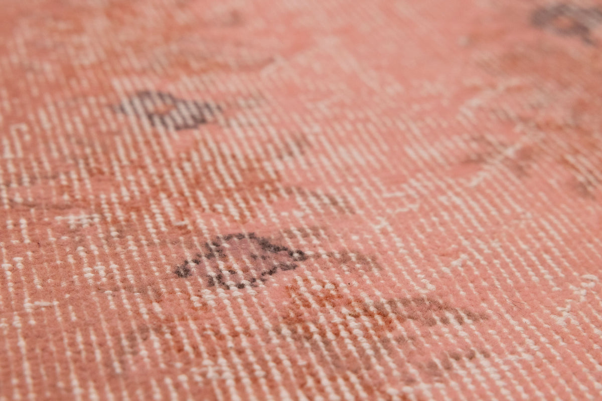 Close-up of a vintage pink overdyed Turkish Isparta wool and cotton rug with faded floral patterns.