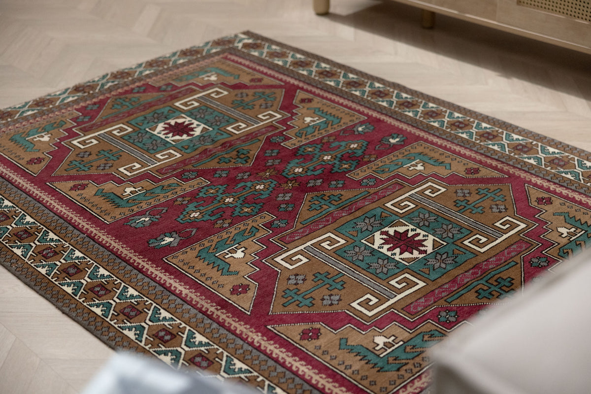 Hand-woven 4x6 ft vintage Kars wool rug featuring geometric patterns in red, brown, and teal on a herringbone floor.