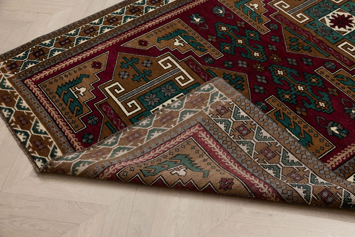 Hand-woven 4x6 ft vintage Turkish wool rug in red and brown with intricate geometric patterns and a folded corner.