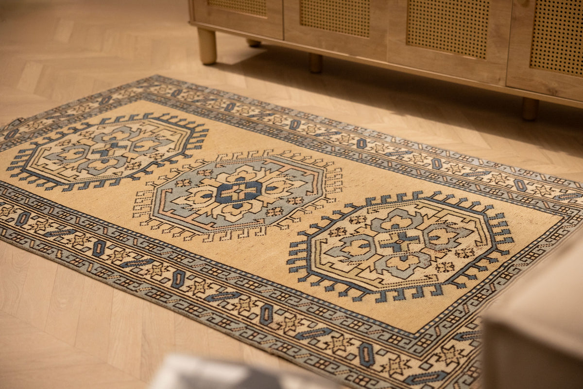 Hand-woven 3x6 ft vintage Oushak wool rug in beige and navy with traditional geometric patterns on a wooden floor.
