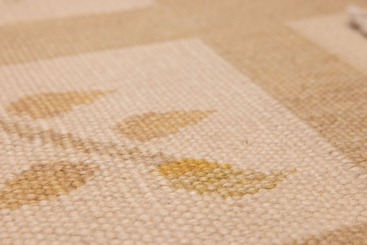Close-up of a hand-woven beige and brown floral vintage Turkish wool-cotton rug with a flatweave texture.