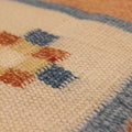 Close-up of a hand-woven vintage Turkish rug featuring orange, beige, and blue geometric patterns in wool and cotton.