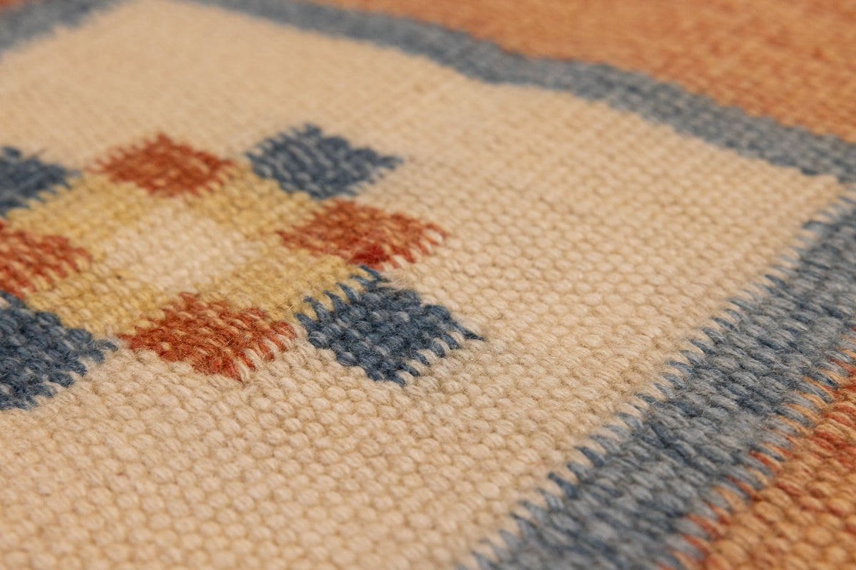 Close-up of a hand-woven vintage Turkish rug featuring orange, beige, and blue geometric patterns in wool and cotton.