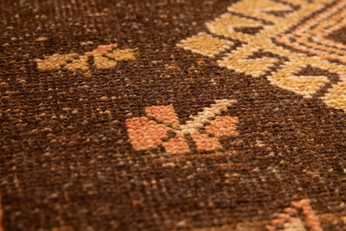 Close-up of a vintage Turkish wool runner rug featuring orange and brown geometric patterns and a textured weave.