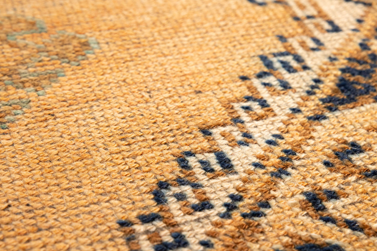 Close-up of a vintage Turkish wool runner rug featuring orange and brown geometric patterns and a textured, handwoven weave.