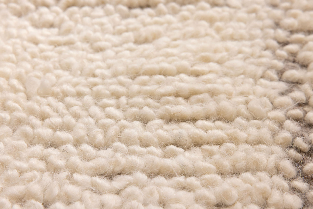 Close-up of a thick, cream-colored handwoven wool shaggy rug with a soft, dense, and textured pile surface.
