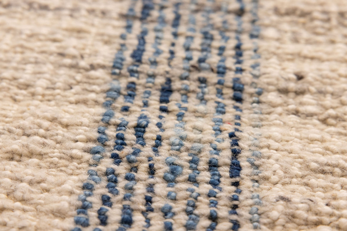 Close-up of a handwoven white and blue striped wool-cotton flatweave rug with a textured, durable finish.