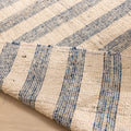Handwoven white and blue striped wool-blend flatweave rug with a folded corner showing reversible texture.
