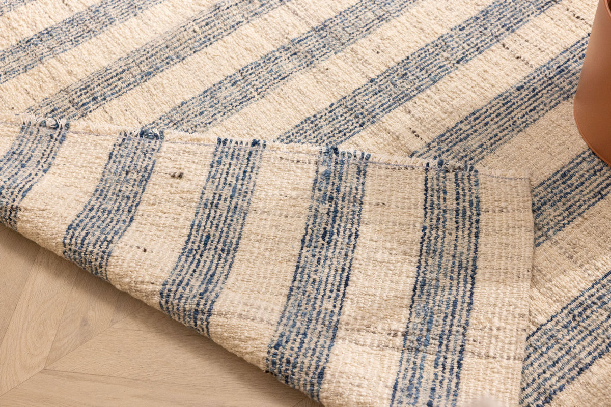 Handwoven white and blue striped wool-blend flatweave rug with a folded corner showing reversible texture.