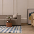 Blue and white checkered wool-blend flatweave rug in a modern living room with a beige sofa and wooden sideboard.