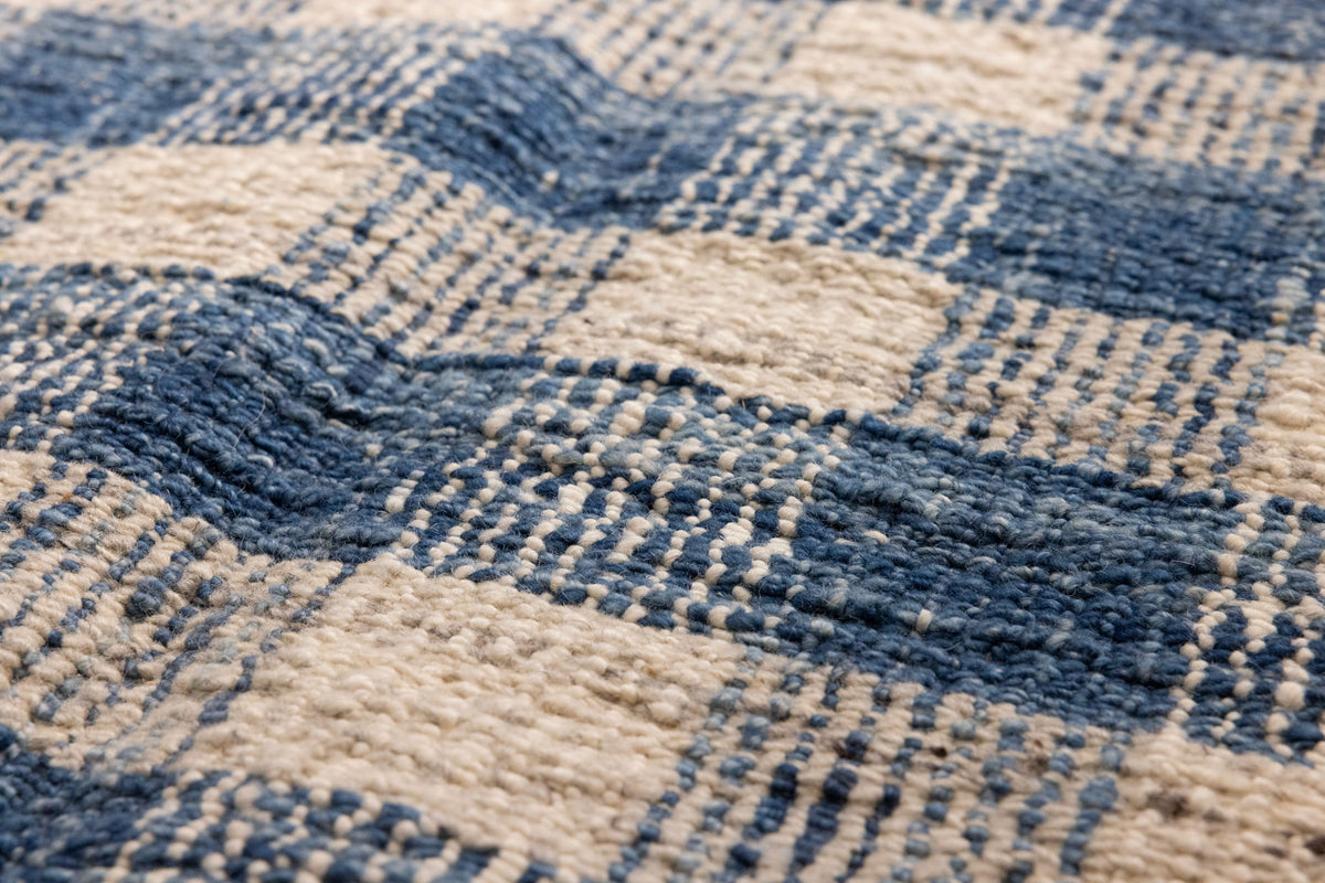 Close-up of a handwoven blue and white checkered wool-blend flatweave rug with a textured, durable finish.