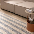 White and blue striped wool-cotton flatweave rug with decorative fringe in a modern living room setting.