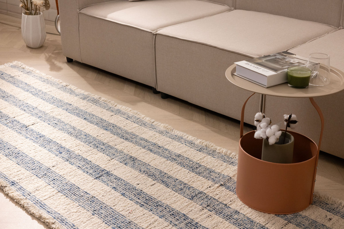 White and blue striped wool-cotton flatweave rug with decorative fringe in a modern living room setting.