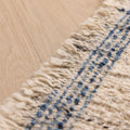 Handwoven white and blue wool-cotton flatweave rug featuring a textured pattern and decorative fringed edge.
