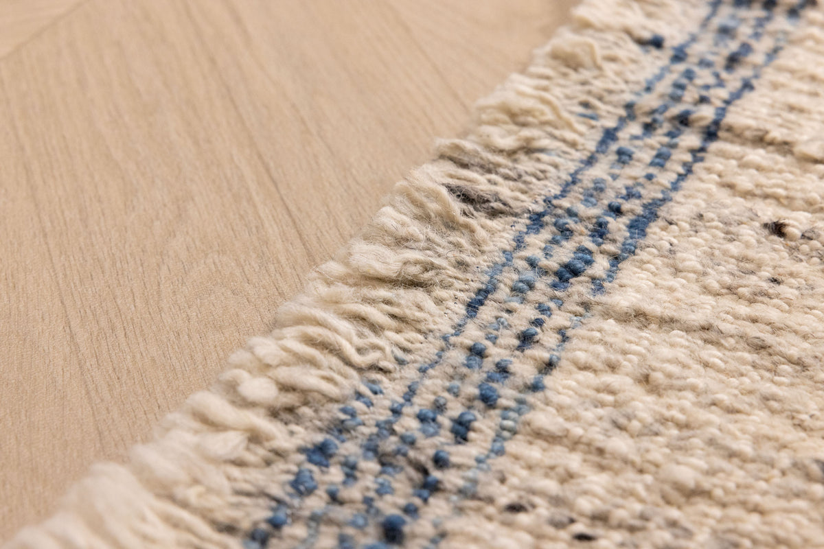 Handwoven white and blue wool-cotton flatweave rug featuring a textured pattern and decorative fringed edge.