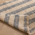 Handwoven white and blue striped wool-blend flatweave rug with decorative fringed edges on a wooden floor.