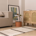 Handwoven white and black wool-blend flatweave rug with striped pattern on a light wood floor in a modern living room.