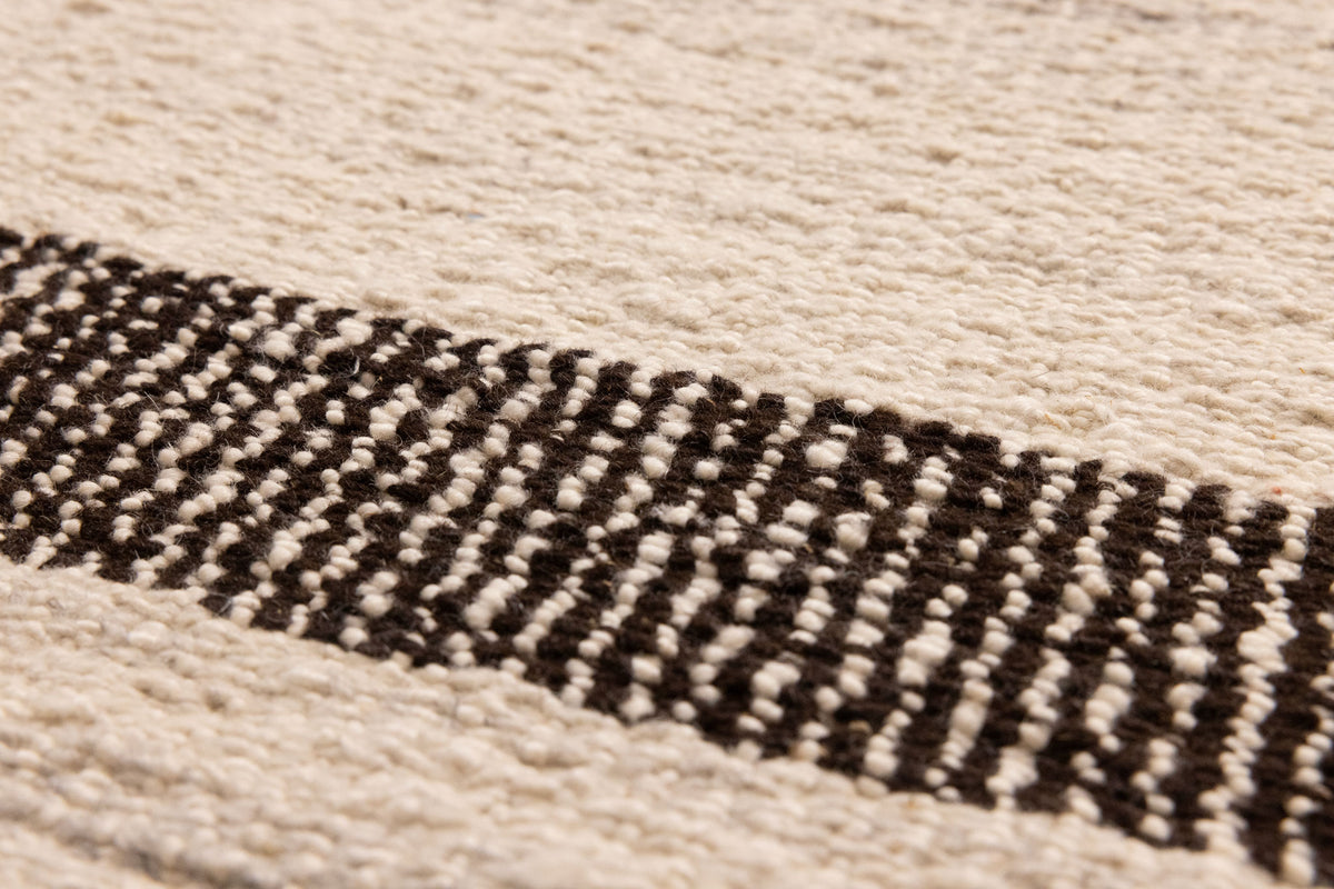 Close-up of a handwoven black and white wool-blend flatweave rug featuring a textured striped pattern.