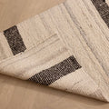 Handwoven black and white wool-blend flatweave rug with a striped pattern, shown folded on a wooden floor.