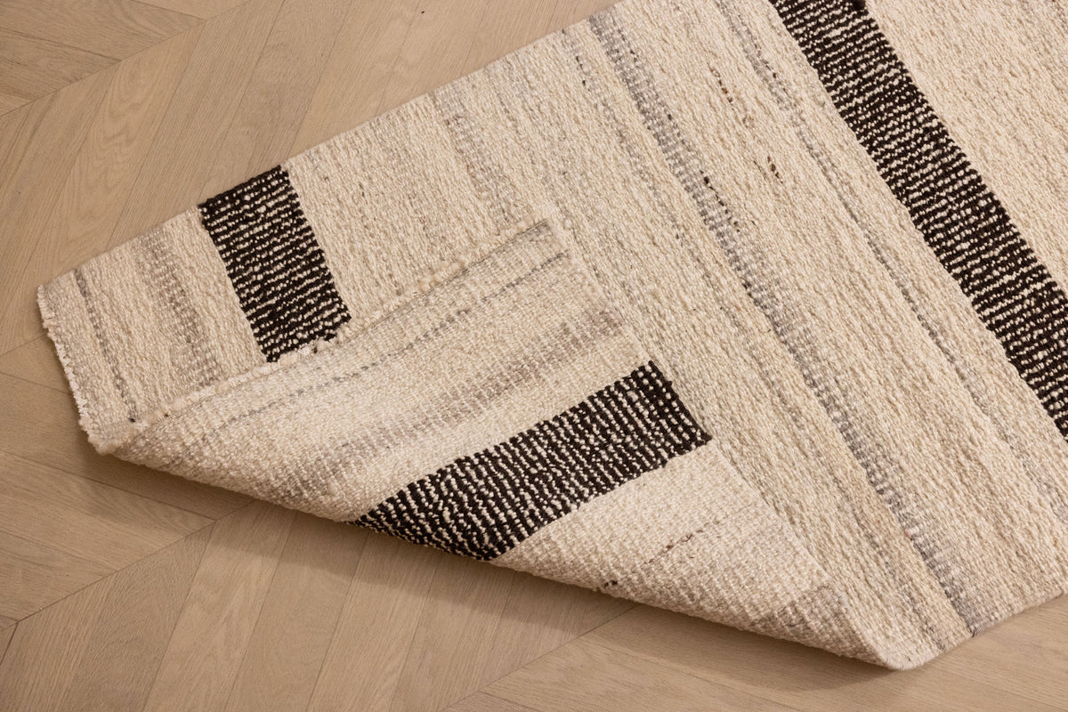 Handwoven black and white wool-blend flatweave rug with a striped pattern, shown folded on a wooden floor.
