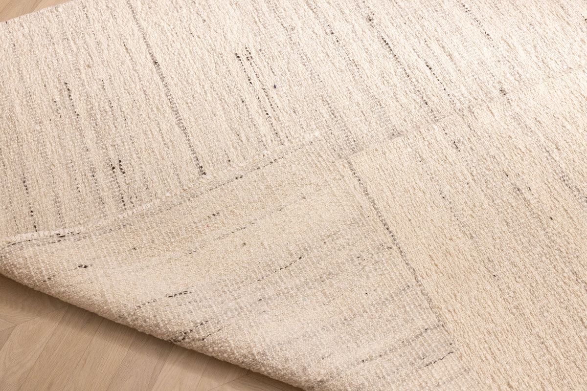 Handwoven white wool and cotton flatweave rug with subtle vertical textured stripes and a folded corner.