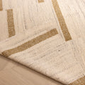 Handwoven white and brown wool-cotton flatweave rug with a modern geometric pattern and a folded corner on a wood floor.