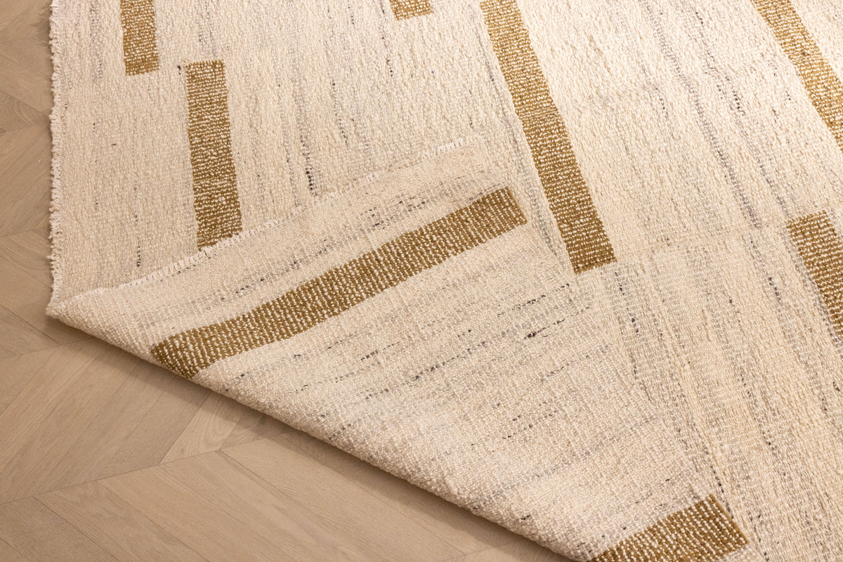 Handwoven white and brown wool-cotton flatweave rug with a modern geometric pattern and a folded corner on a wood floor.