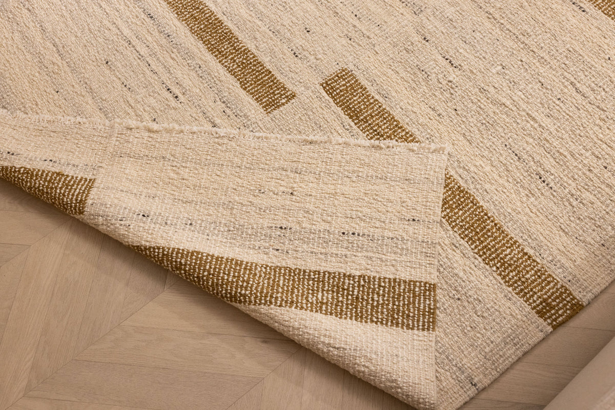 Beige and brown handwoven wool-blend flatweave rug with a striped geometric pattern and a folded corner.