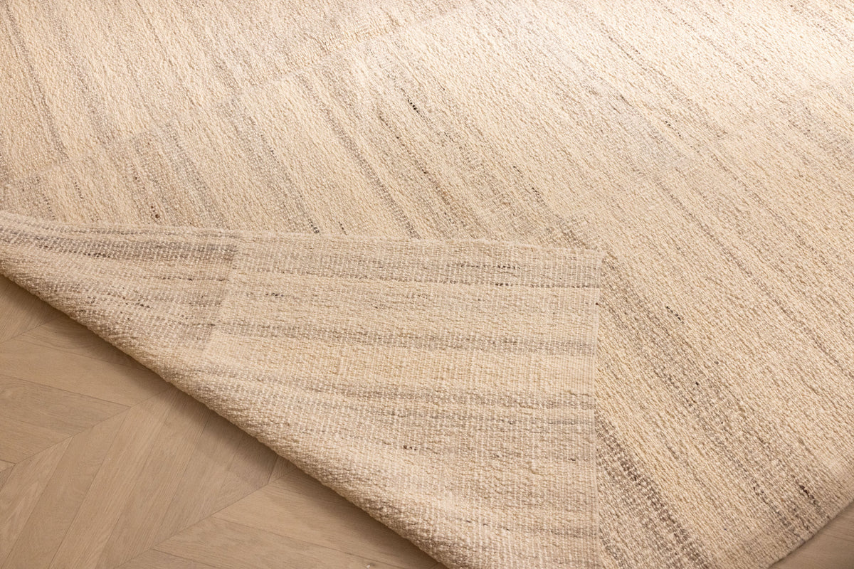 Handwoven white wool and cotton flatweave rug with a textured striped pattern and a folded corner on wood flooring.