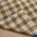 Handwoven white, brown, and blue checkered wool-blend flatweave rug with a folded corner showing texture.