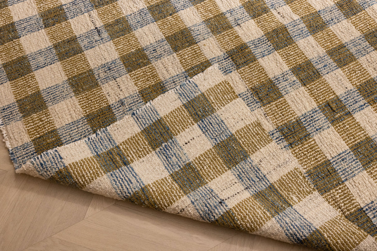 Handwoven white, brown, and blue checkered wool-blend flatweave rug with a folded corner showing texture.