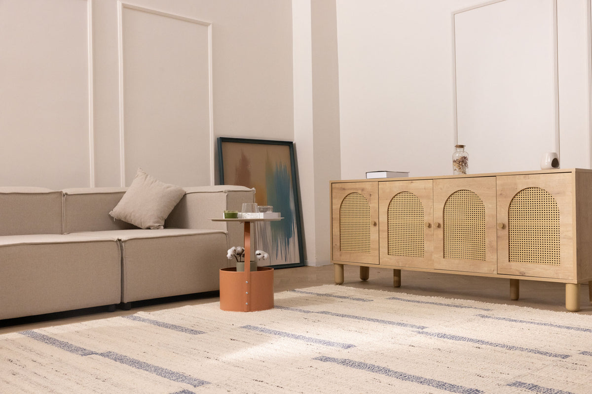 Handwoven white and blue wool-blend flatweave rug in a modern living room with a beige sofa and rattan sideboard.