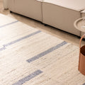 Handwoven white and blue wool-blend flatweave rug with a modern striped pattern in a bright living room setting.
