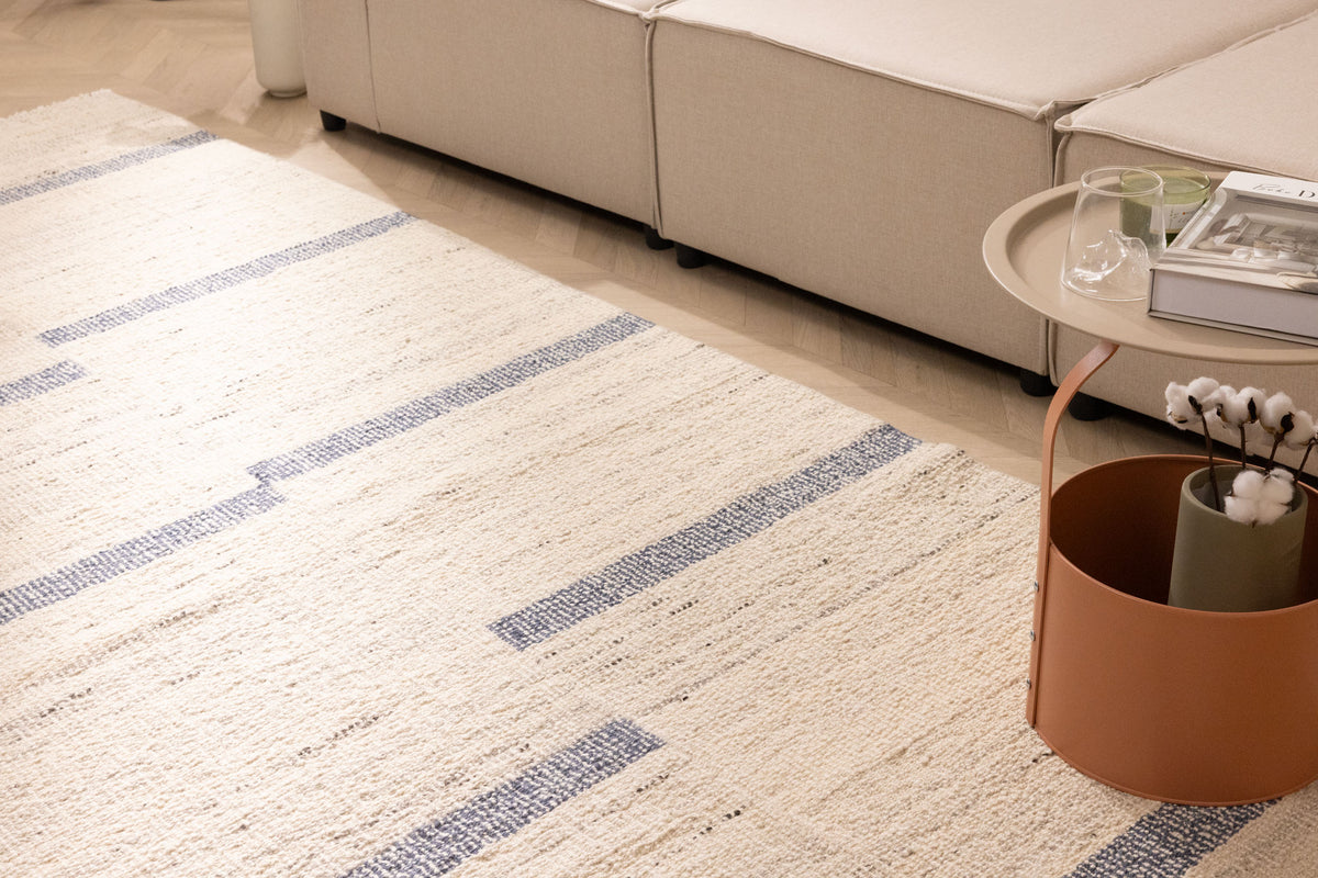 Handwoven white and blue wool-blend flatweave rug with a modern striped pattern in a bright living room setting.