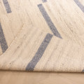 Handwoven white and blue wool-blend flatweave rug with a striped pattern, shown with a folded corner on a wooden floor.