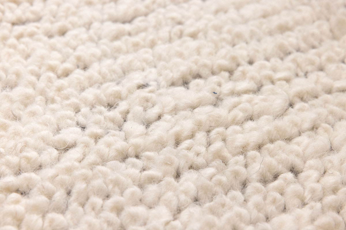 Close-up of a thick, cream-colored shaggy wool rug with a soft, handwoven high-pile texture.