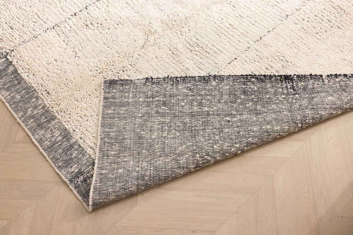 Handwoven black and white shaggy wool rug with a thick, textured pile and durable cotton backing on a wooden floor.