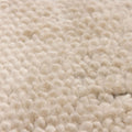 Close-up of a soft, cream-colored shaggy wool rug with a dense, handwoven high-pile texture.