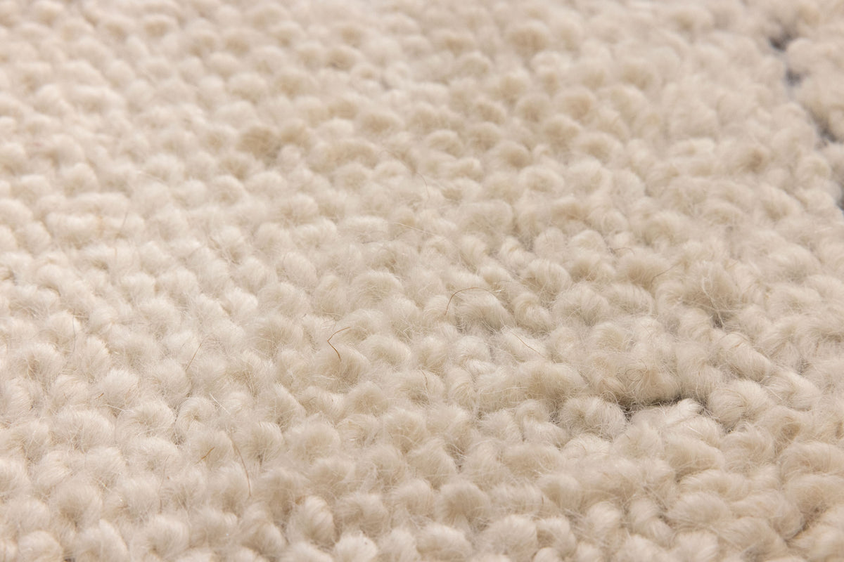 Close-up of a soft, cream-colored shaggy wool rug with a dense, handwoven high-pile texture.