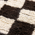 Close-up of a handwoven shaggy wool rug featuring a thick, soft black and cream checkered pattern.