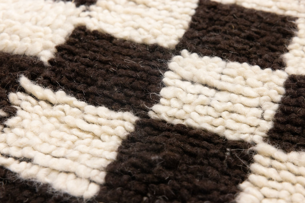 Close-up of a handwoven shaggy wool rug featuring a thick, soft black and cream checkered pattern.