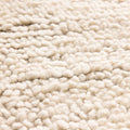 Close-up of a cream-colored, handwoven shaggy wool rug with a thick, soft, and textured high-pile surface.