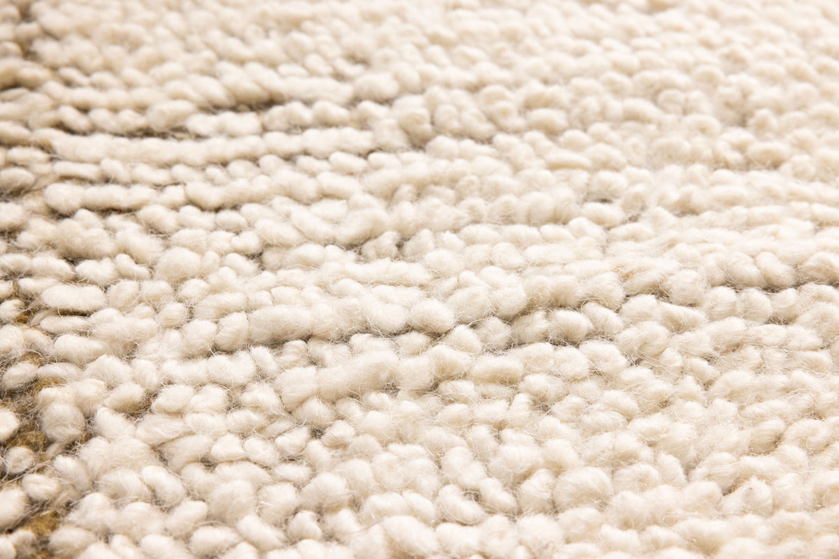 Close-up of a cream-colored, handwoven shaggy wool rug with a thick, soft, and textured high-pile surface.