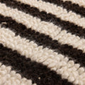 Close-up of a handwoven shaggy wool rug featuring a textured black and cream striped pattern.