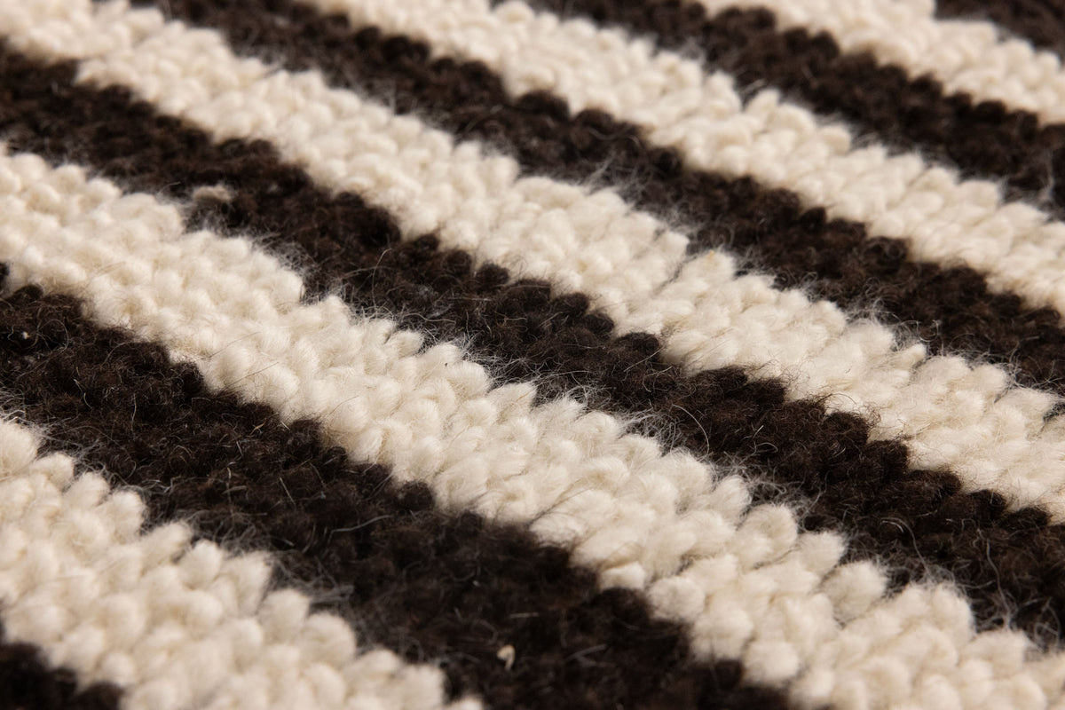 Close-up of a handwoven shaggy wool rug featuring a textured black and cream striped pattern.
