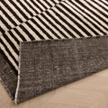 Handwoven black and white striped shaggy wool rug with a durable cotton backing on a light wood floor.
