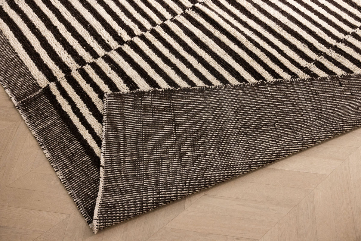 Handwoven black and white striped shaggy wool rug with a durable cotton backing on a light wood floor.